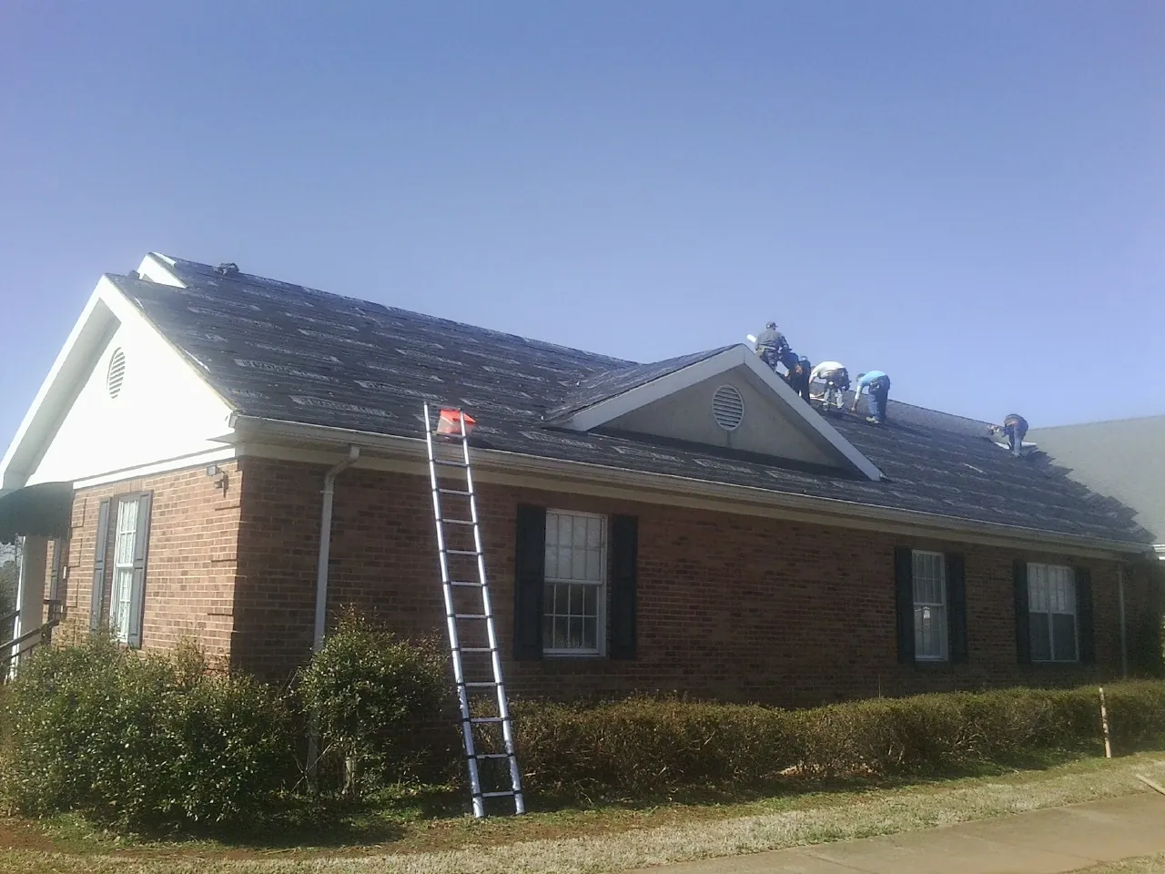 Crew tearing shingles off a brick ranch roof with a ladder set — Emergency Roof Repair work by our crew in Cross Plains