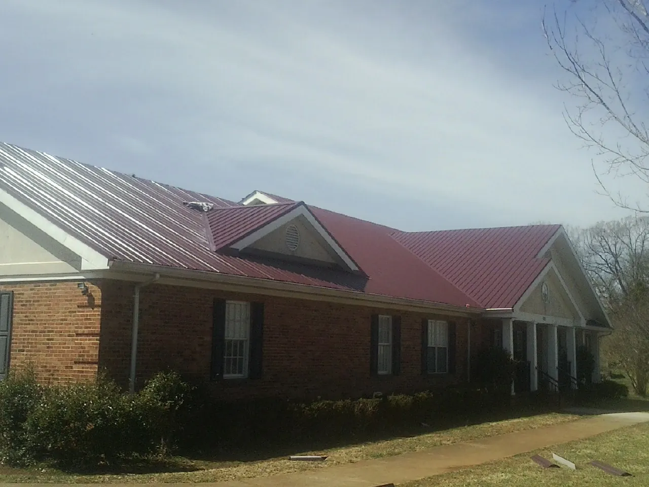Red metal roof with gabled entries on a long brick building, from a Hail Damage Roof Repair job in Cross Plains
