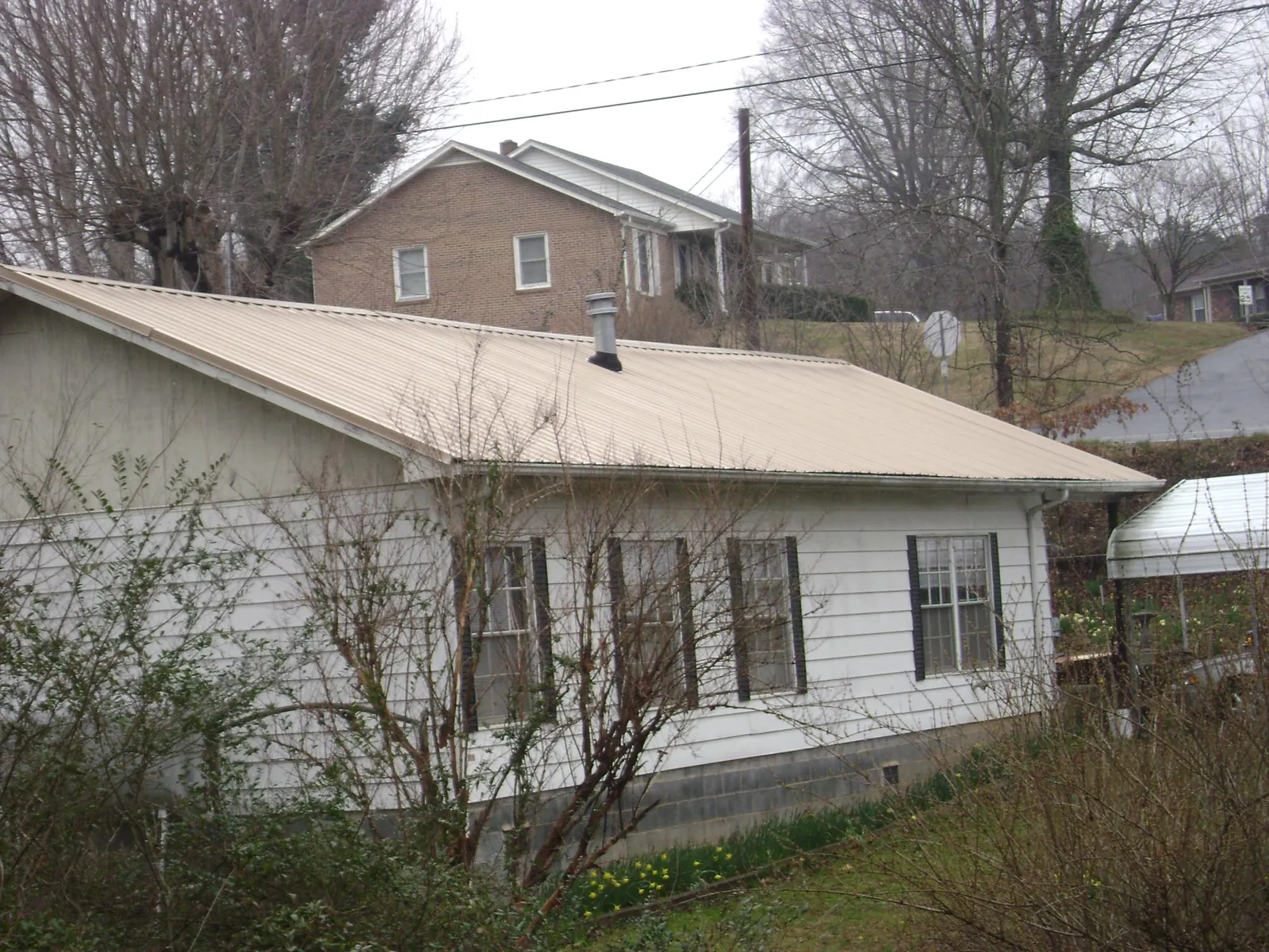 Tan metal roof on a white sided house set into a hillside — Commercial Roofing by Roofing Brothers in Cross Plains